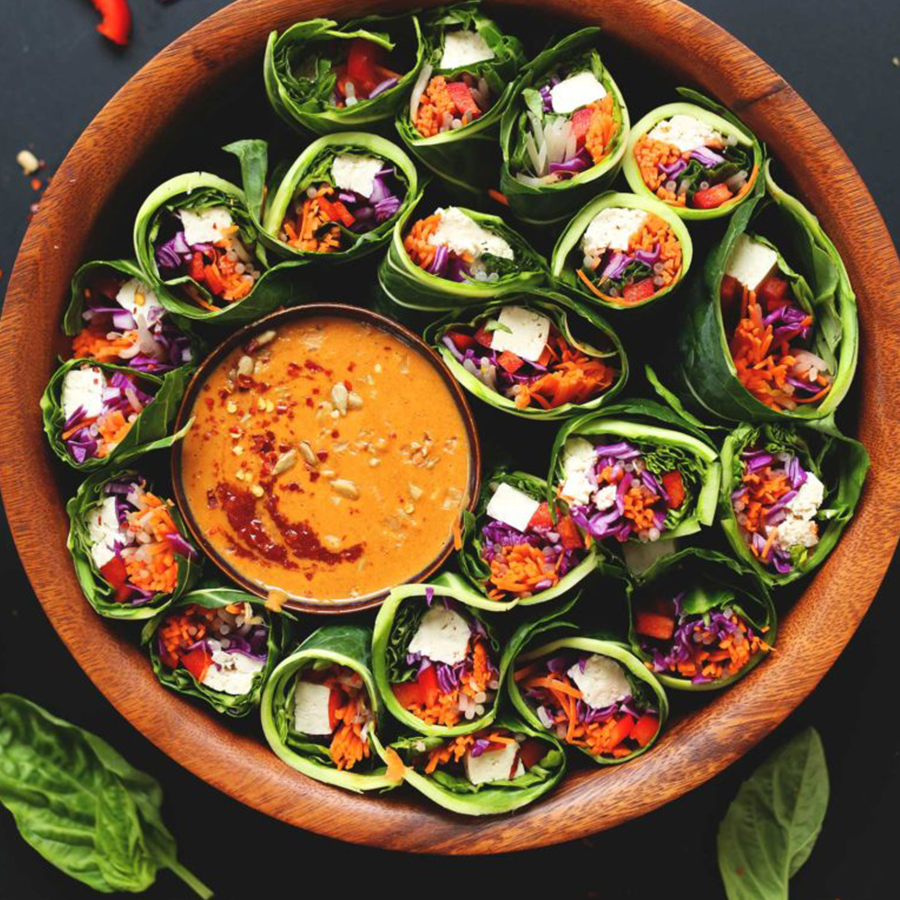 Wood bowl filled with halved homemade salad rolls and peanut sauce for dipping