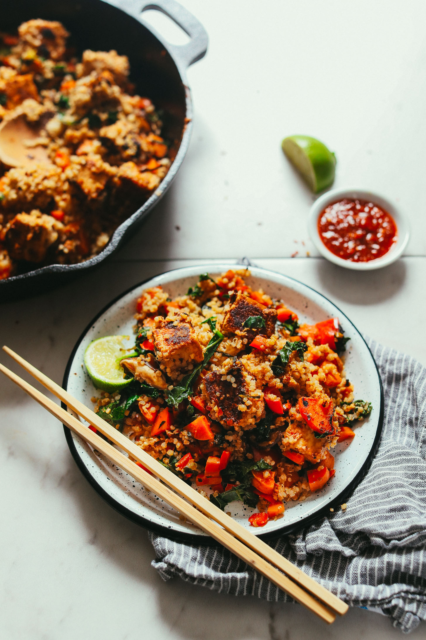 Image of tempeh stir fry served on a white plate with chopsticks and a cast iron pan in the background