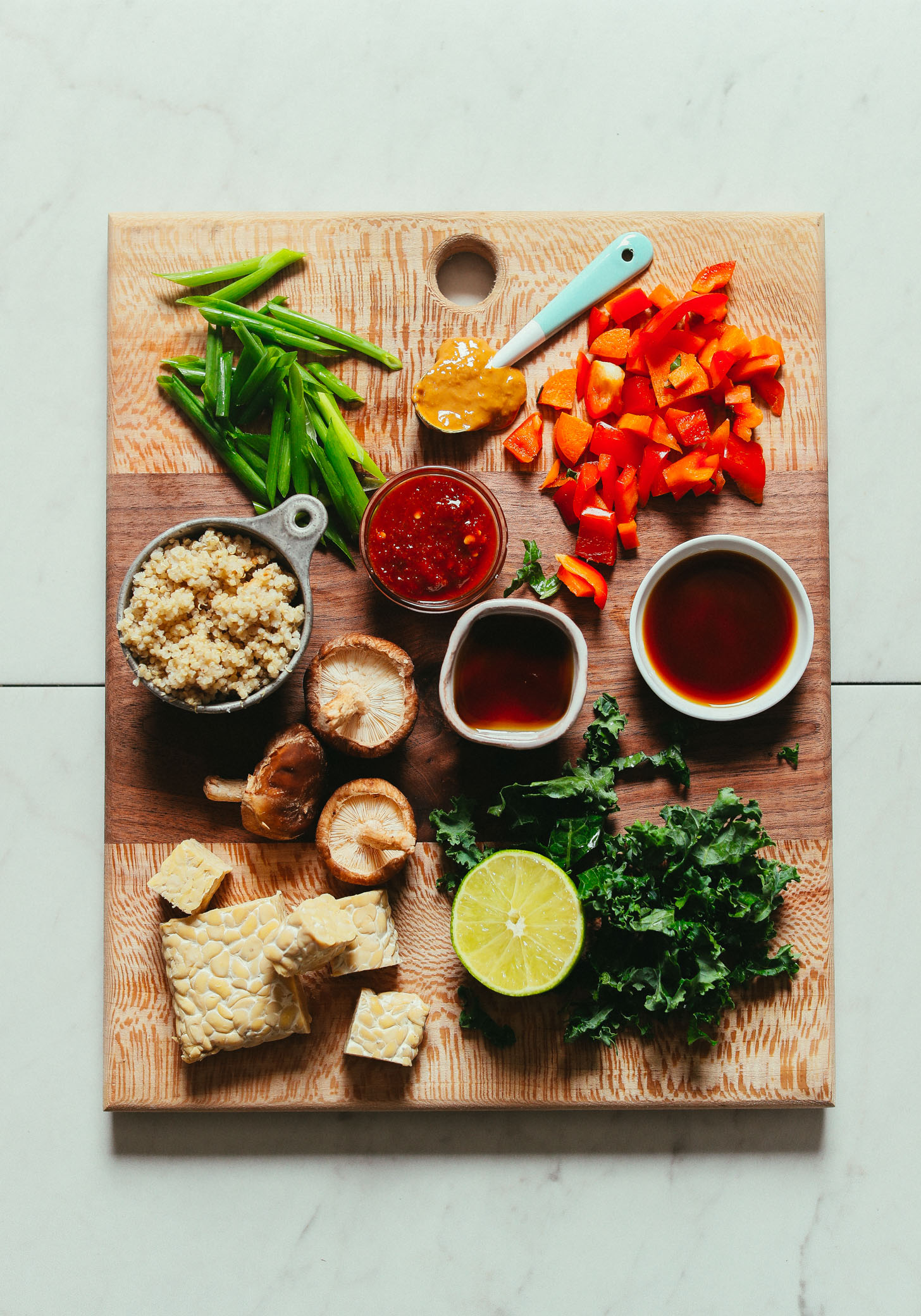 Overhead image of cutting board with ingredients for a tempeh stir fry including tempeh quinoa bell pepper green onion and kale