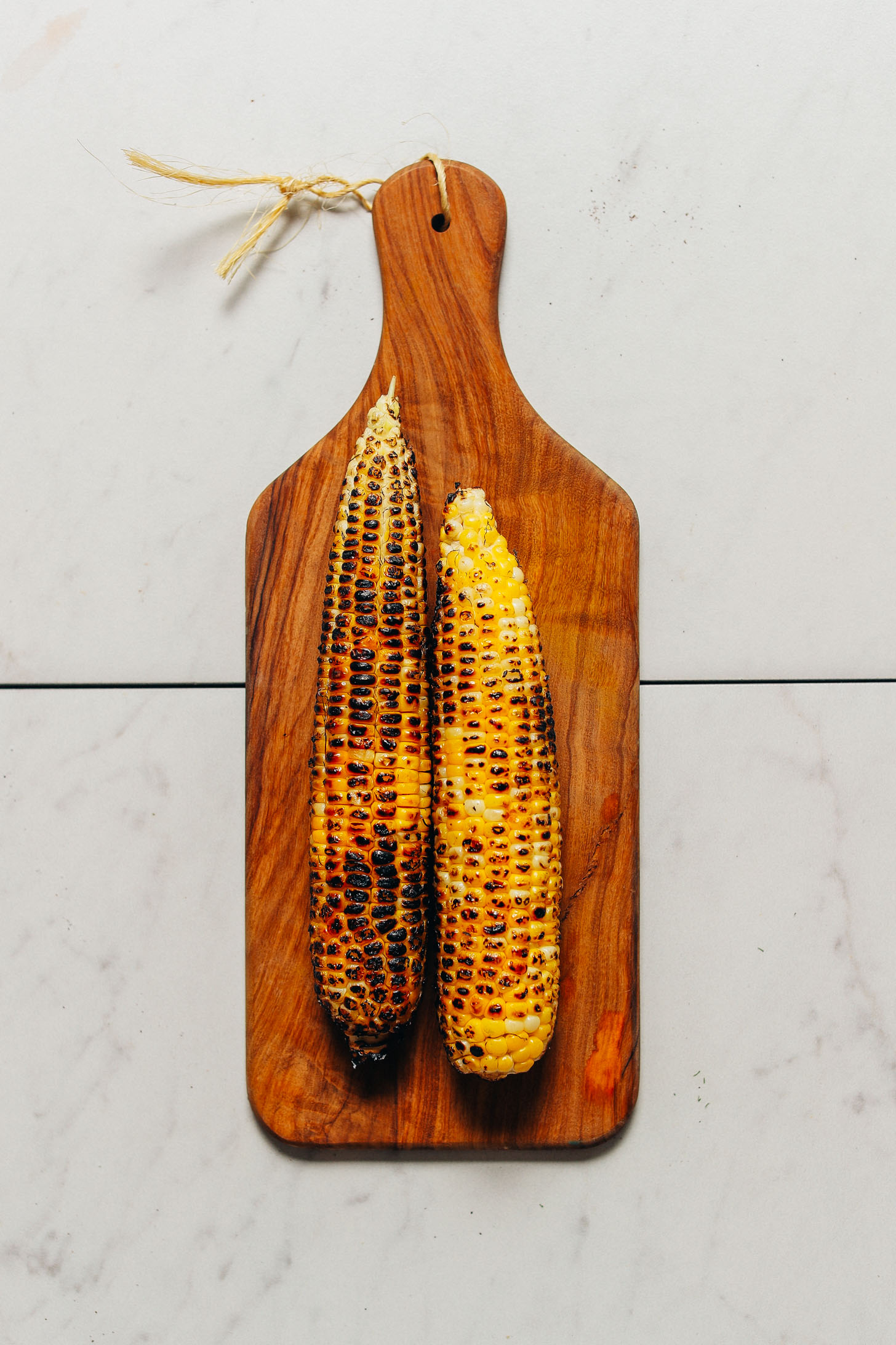 Two ears of grilled corn on a wood cutting board