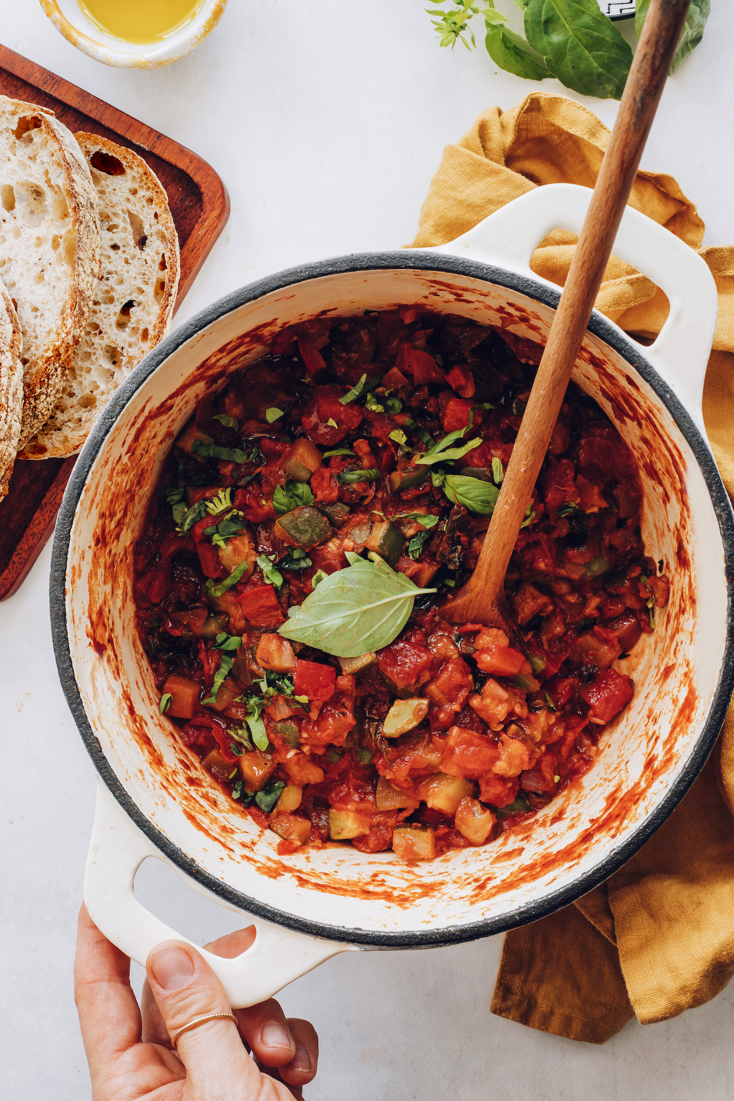 Holding the handle of a Dutch oven with ratatouille topped with fresh basil