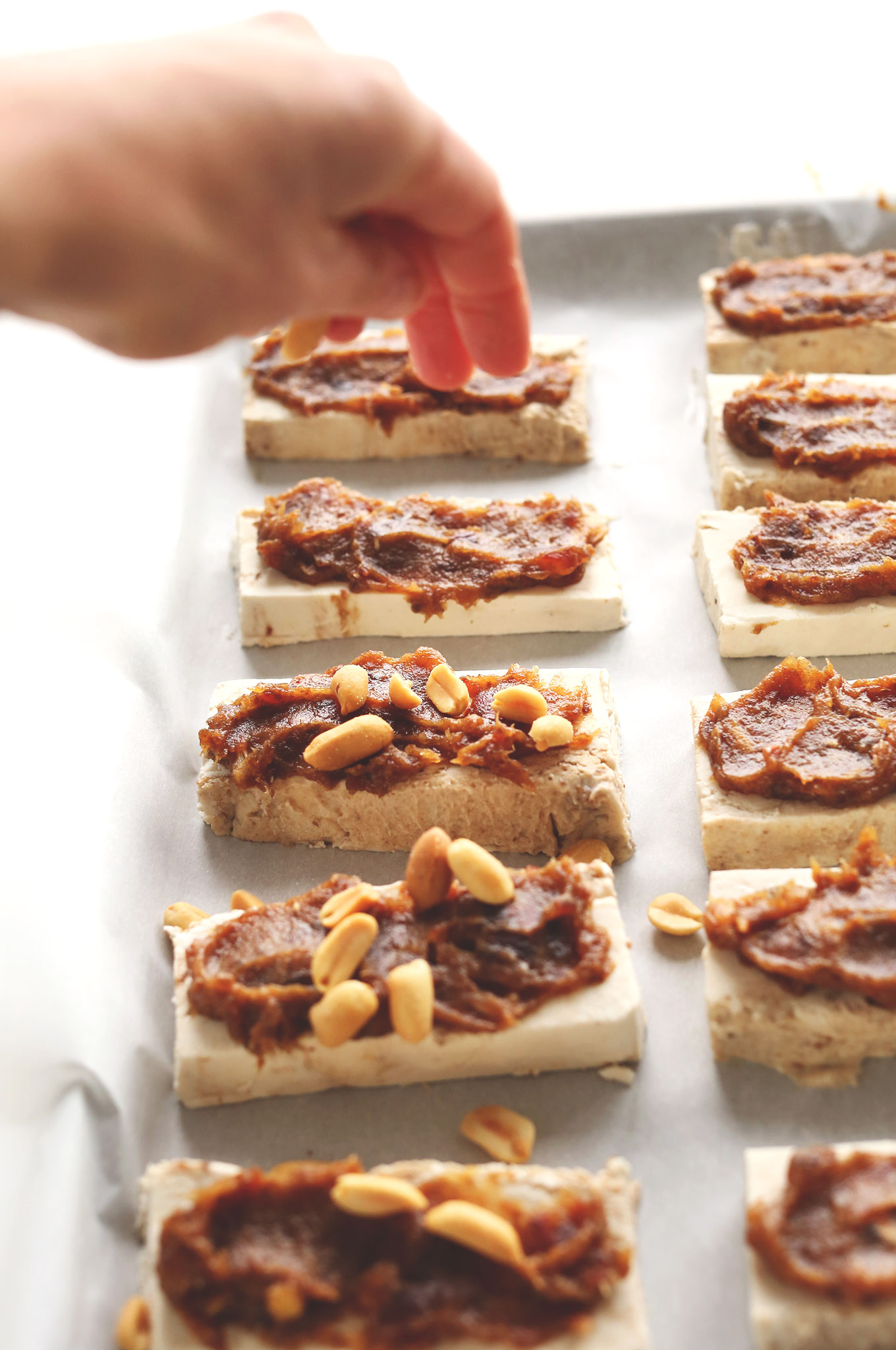 Sprinkling peanuts onto slabs of vegan ice cream and date caramel for homemade Vegan Ice Cream Snickers Bars