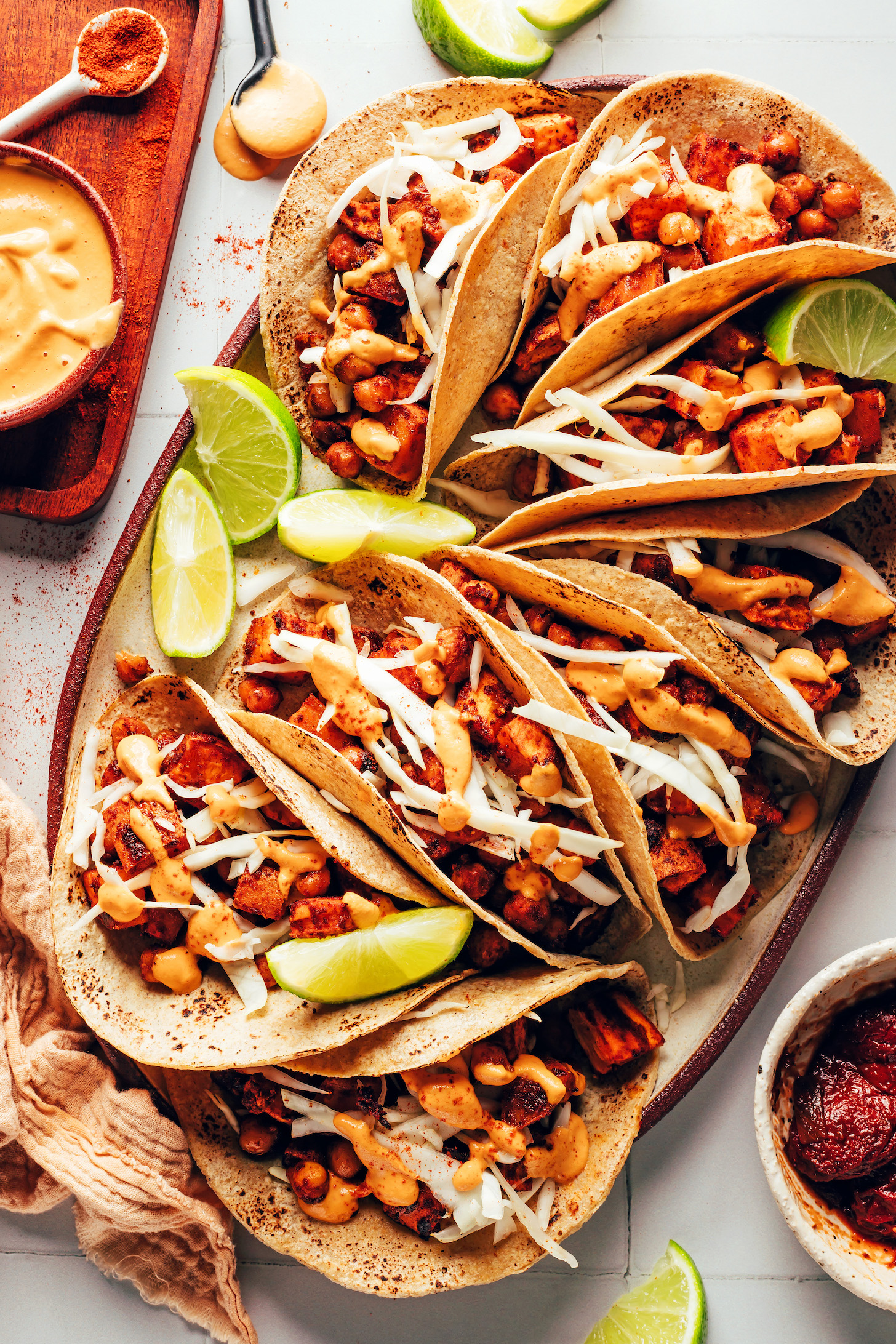 Platter of sweet potato chickpea tacos with cabbage, chipotle crema, and lime wedges