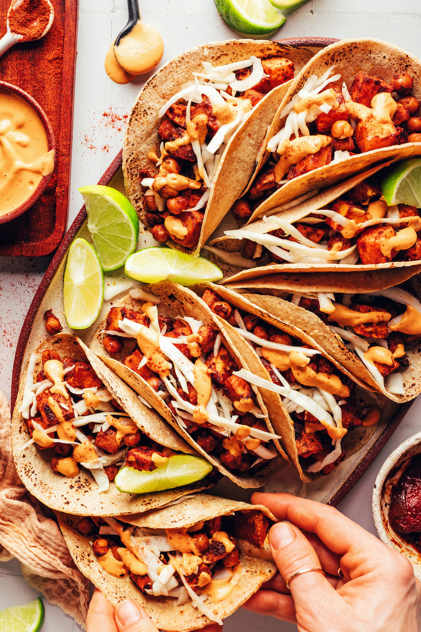 Hand reaching in to pick up a BBQ sweet potato chickpea taco from a platter