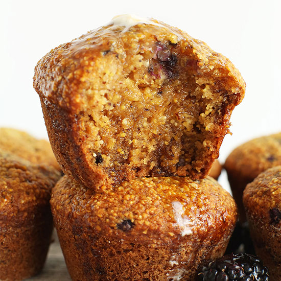 Stack of Vegan Blackberry Cornmeal Muffins with the top one partially eaten