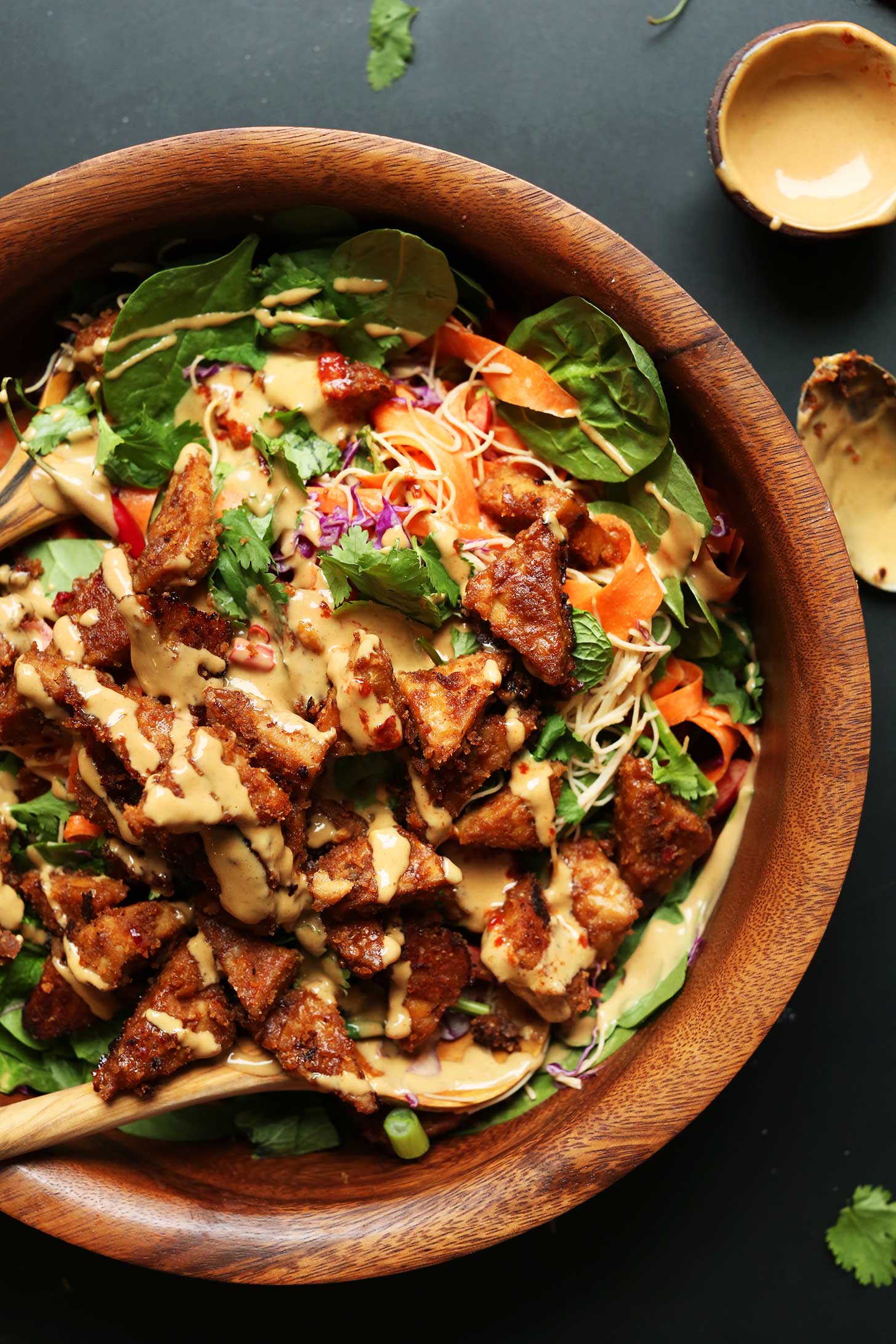 Beautiful wood bowl full of Thai Salad with Marinated Peanut Tempeh topped with our easy peanut sauce recipe