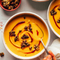 Holding a spoon in a bowl of creamy vegan carrot ginger soup