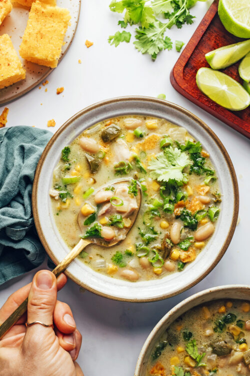 Bowls of white bean chicken chili next to lime wedges and cilantro