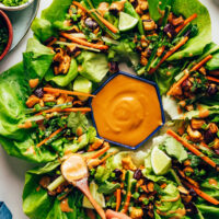 Drizzling a savory sesame sauce onto tofu and eggplant lettuce cups