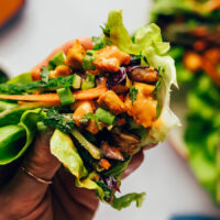 Holding up a lettuce cup filled with crispy baked tofu, roasted eggplant, fresh veggies and herbs, and a sauce