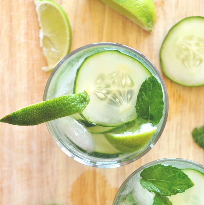 Glasses of our Cucumber Cooler Cocktail recipe topped with cucumbers slices, mint leaves, and limes