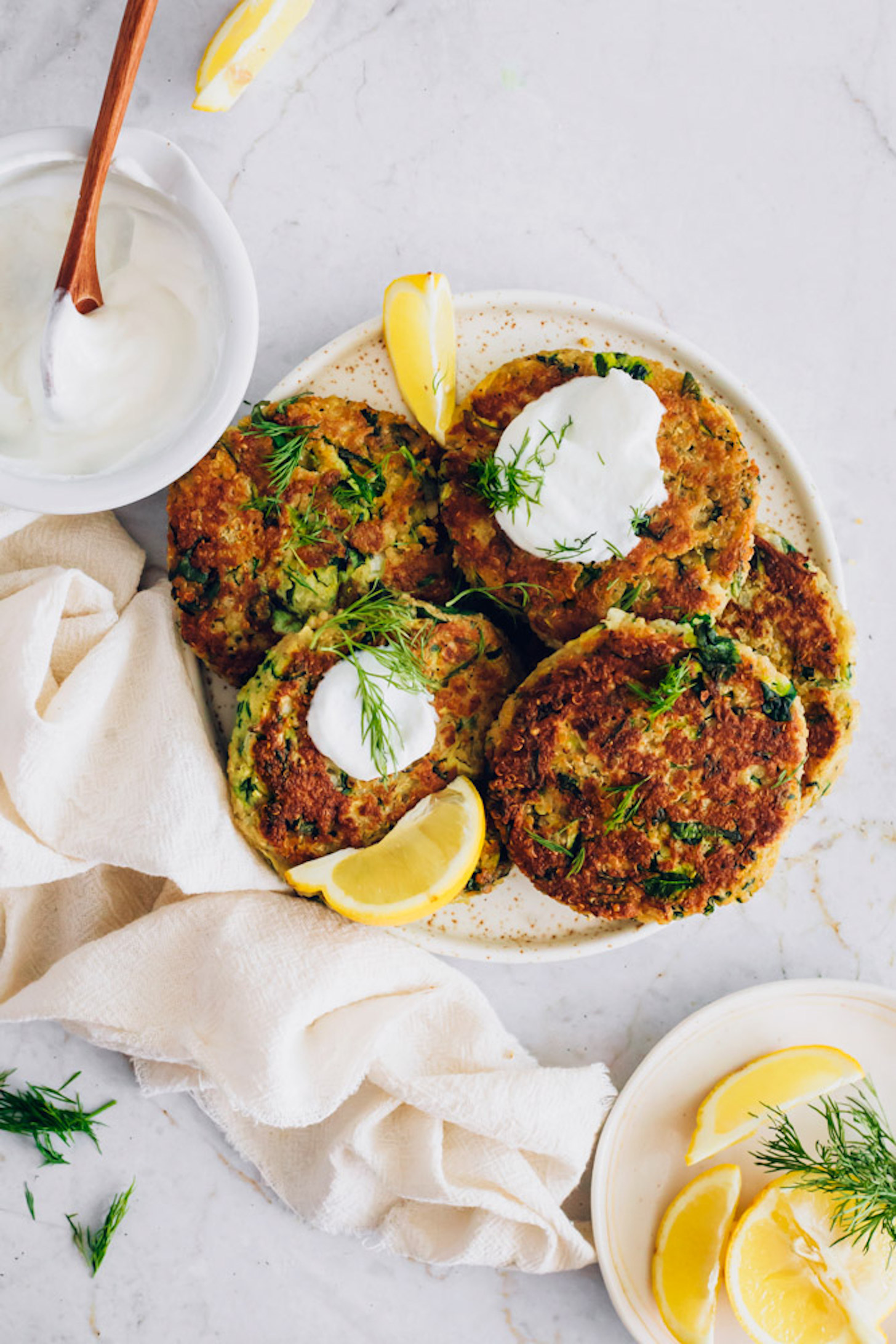 Bowl of coconut yogurt and plate of lemon wedges next to a plate of Vegan Zucchini Fritters