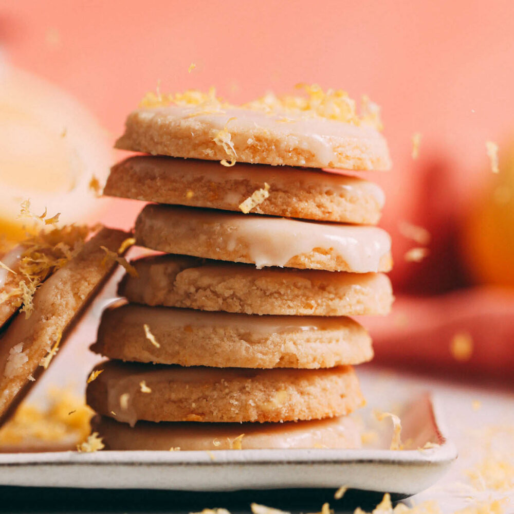 Lemon zest falling onto a stack of gluten-free vegan lemon cookies