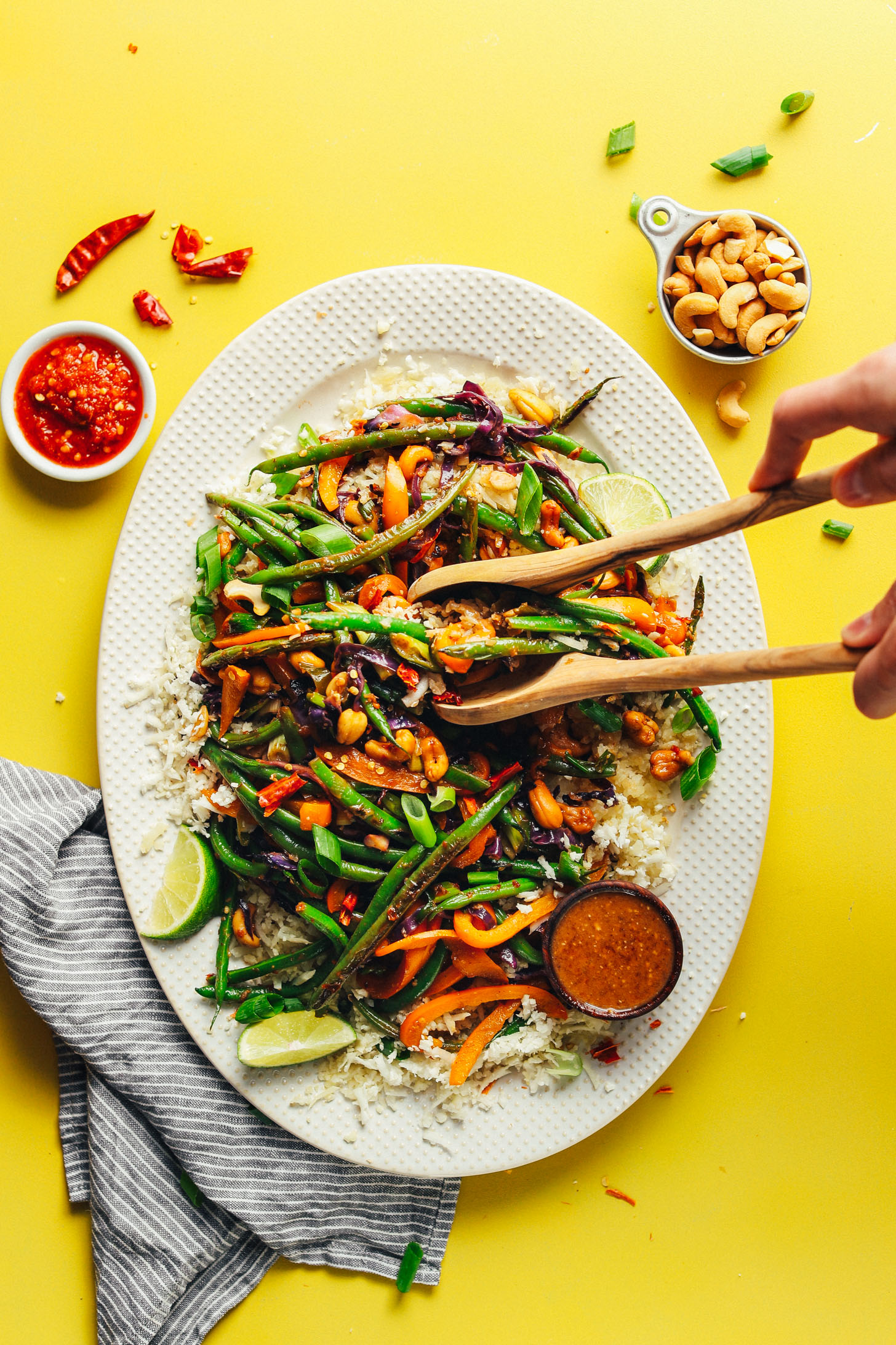 Using wooden salad tongs to grab Weeknight Cauliflower Rice Stir Fry off of a large serving platter