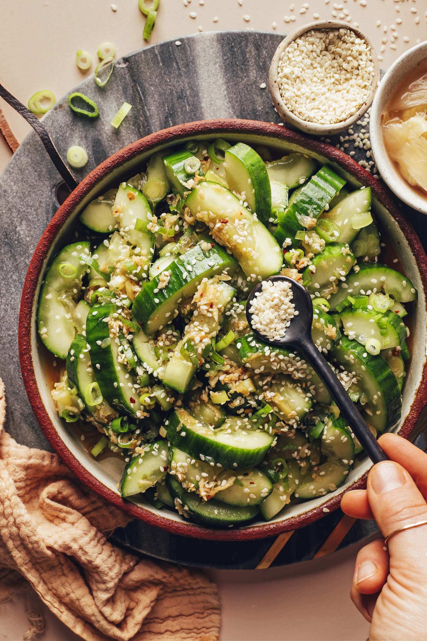 Sprinkling sesame seeds over a smashed cucumber salad