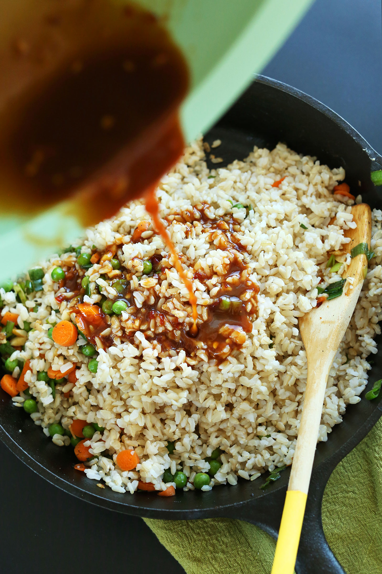 Pouring sauce into a skillet of Vegan Fried Rice with Crispy Tofu