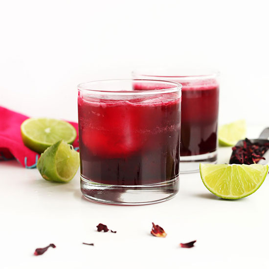 Two glasses of homemade Vegan Hibiscus Margaritas beside lime wedges