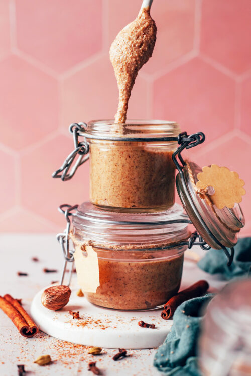 Chai-spiced cashew almond butter falling off a spoon into a jar stacked on another jar of nut butter