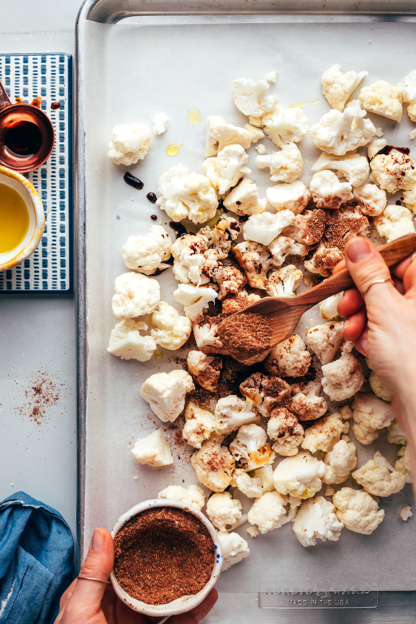 Sprinkling a Jamaican jerk dry rub onto small pieces of cauliflower on a baking sheet