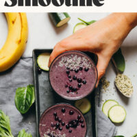 Hand holding a glass of our creamy zucchini blueberry smoothie recipe