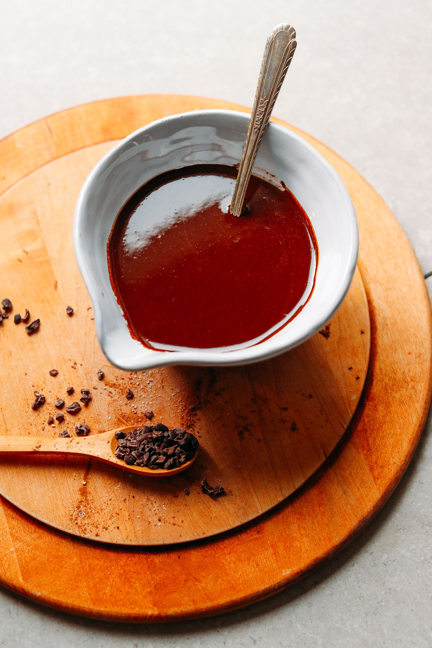 Bowl of melted dark chocolate alongside a spoonful of cacao nibs