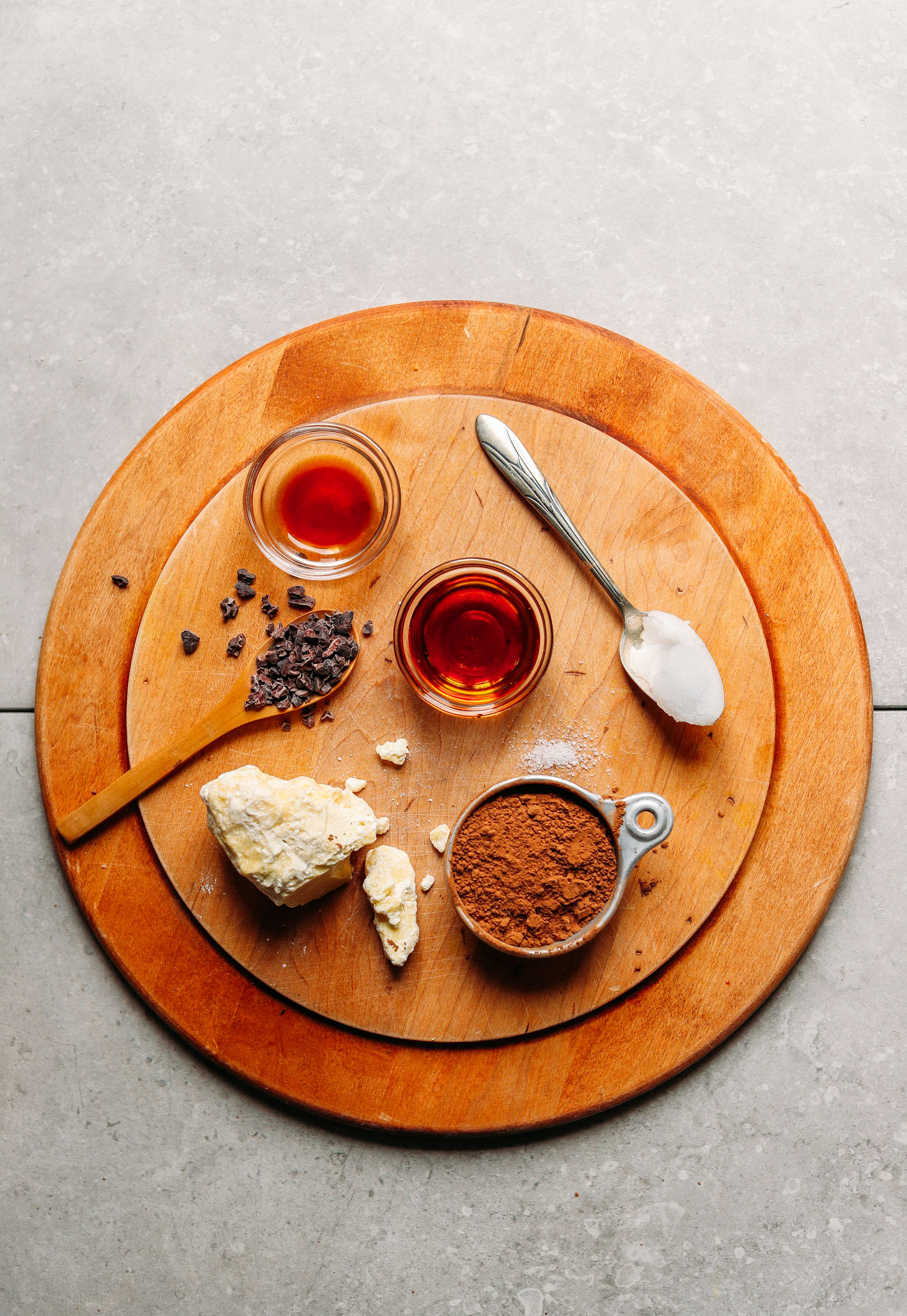 Wood platter featuring cocoa butter, cacao powder, coconut oil, maple syrup, salt, vanilla extract, and cacao nibs for making DIY Vegan Dark Chocolate