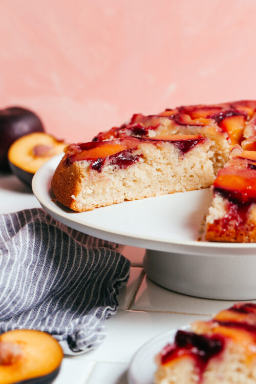 Partially sliced plum upside down cake on a cake stand