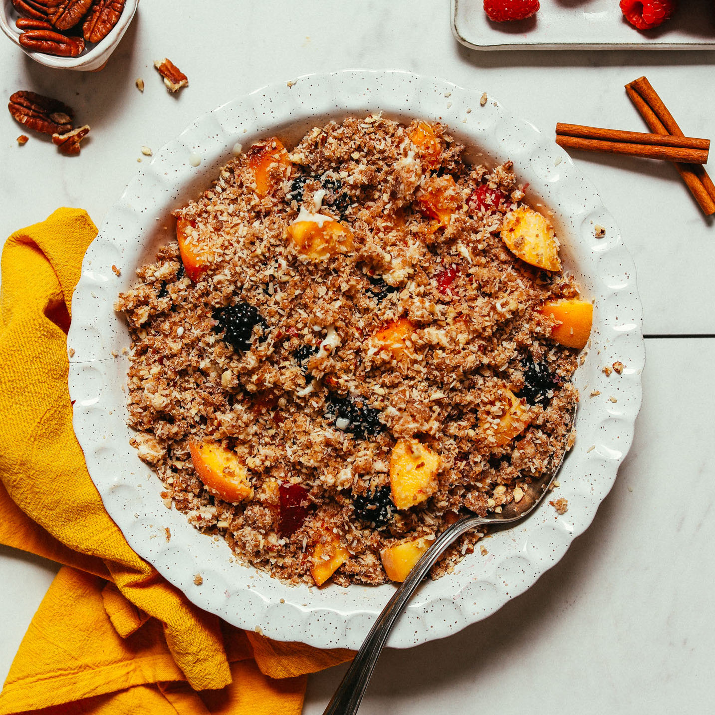 Spoon resting in a pie pan of Peach Blackberry Crisp for a simple raw vegan dessert