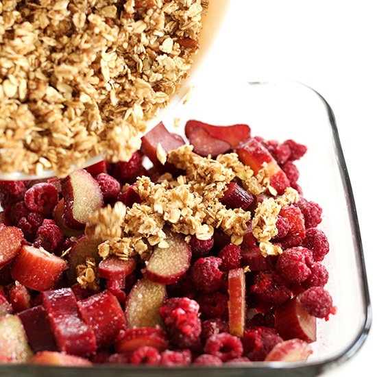 Spreading gluten-free crisp topping onto a baking dish of Vegan Raspberry Rhubarb Crisp