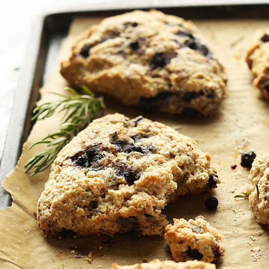 Parchment-lined baking sheet with homemade Rosemary Blueberry Scones and fresh rosemary sprigs