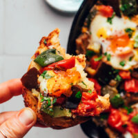 Holding a slice of bread topped with skillet ratatouille and eggs