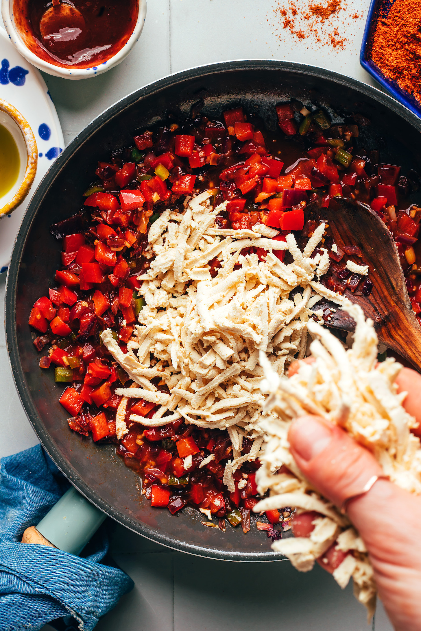 Adding shredded tofu into a skillet of sautéed peppers and onions