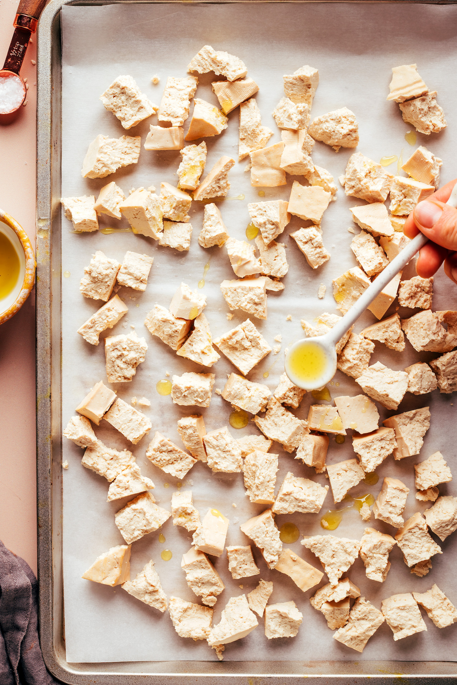 Drizzling oil over a baking sheet of tofu pieces