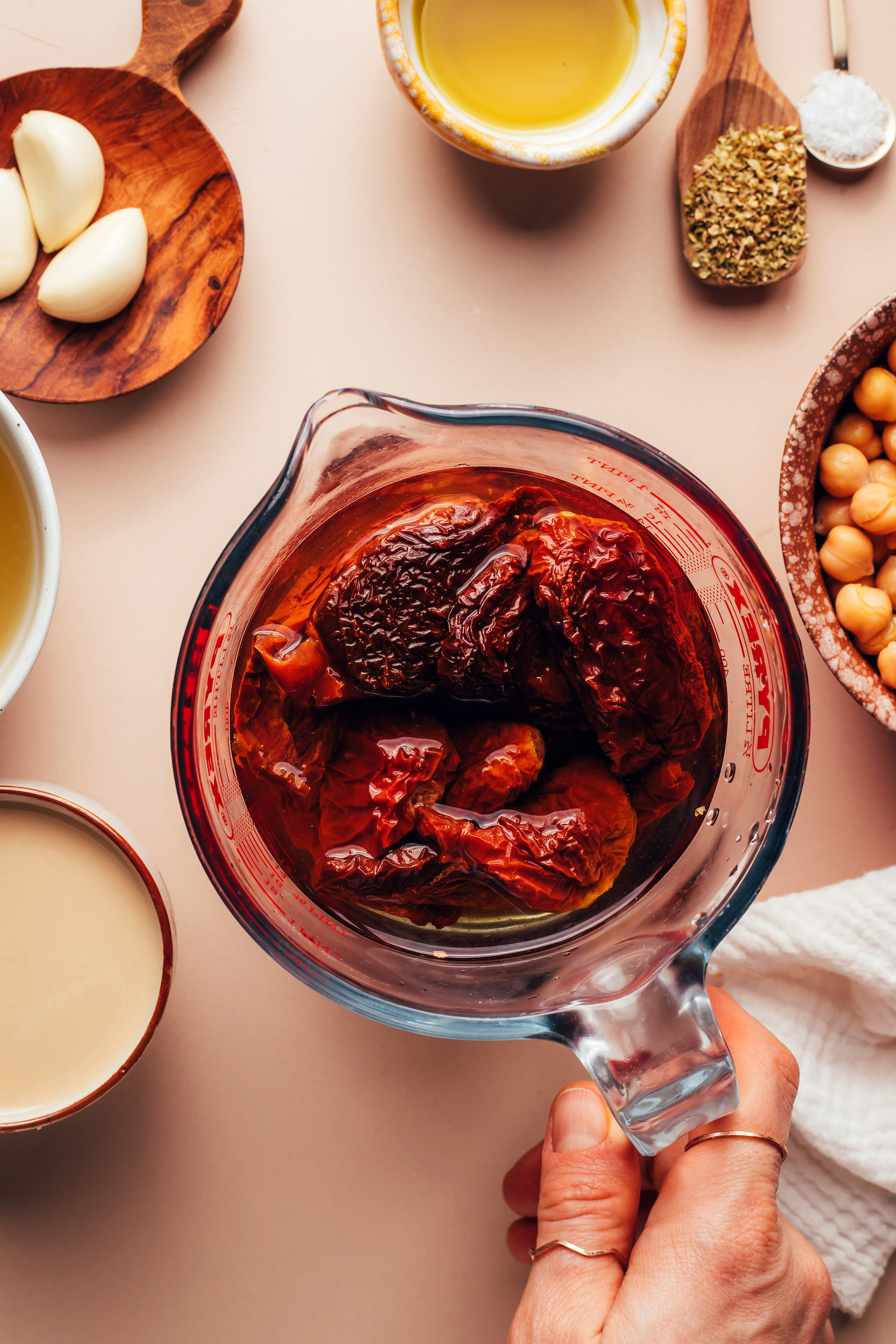 Sun-dried tomatoes soaking in a liquid measuring cup with other ingredients around it