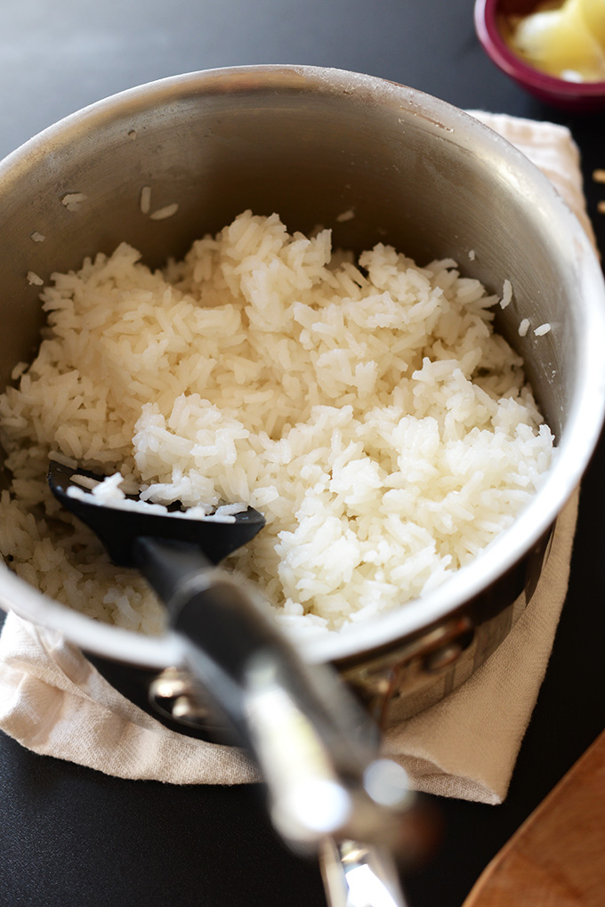 backlit view of white rice cooked in a saucepan with a spatula scooping some rice.