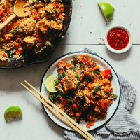 Plate and skillet of Tempeh Veggie Stir Fry with chili sauce and fresh limes