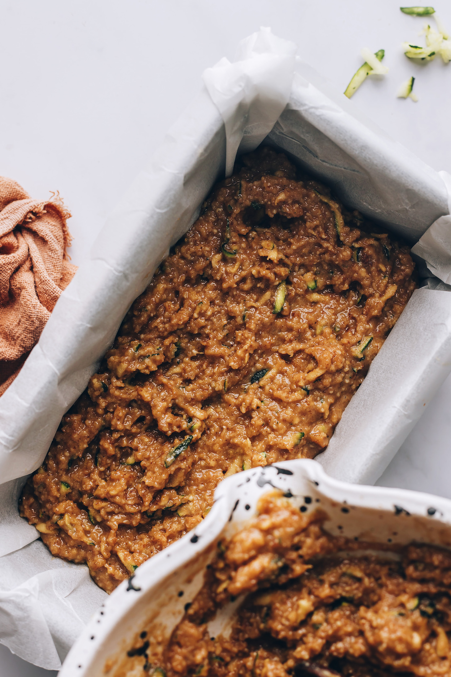 Pouring batter from a mixing bowl into a parchment-lined loaf pan