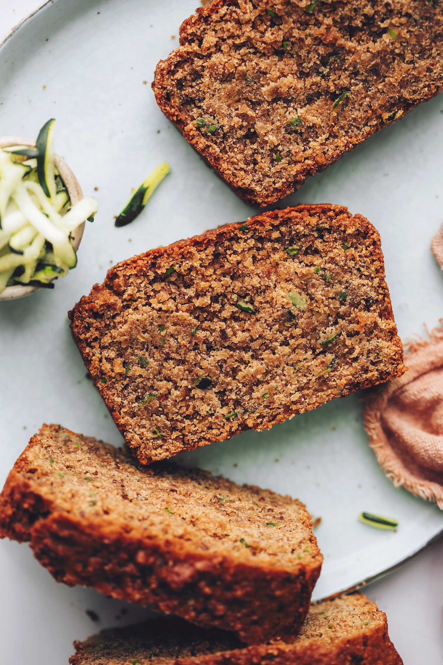 Shredded zucchini next to slices of vegan gluten-free zucchini bread