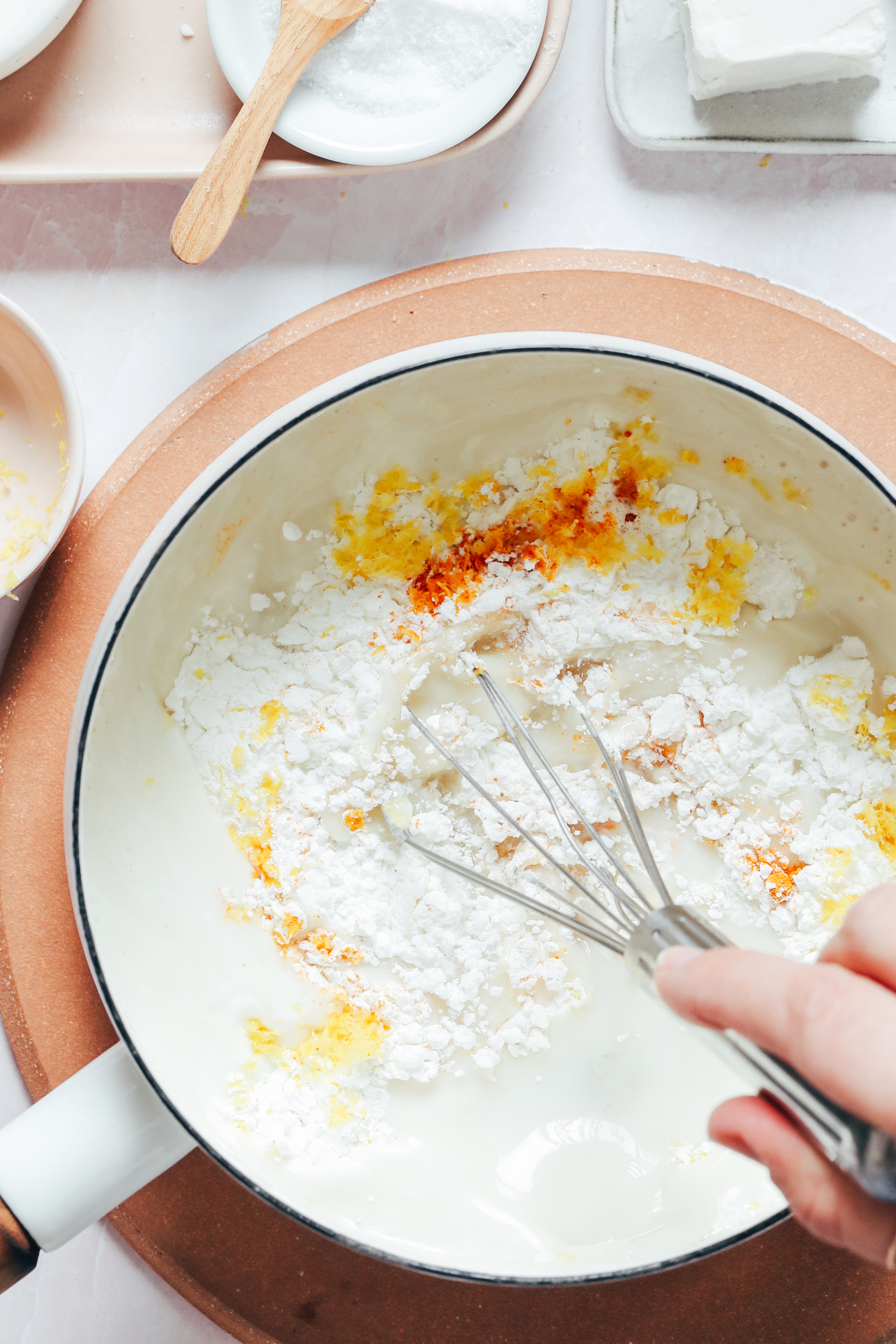 Whisking together cane sugar, cashew milk, lemon juice, lemon zest, cornstarch, turmeric, and sea salt in a white saucepan