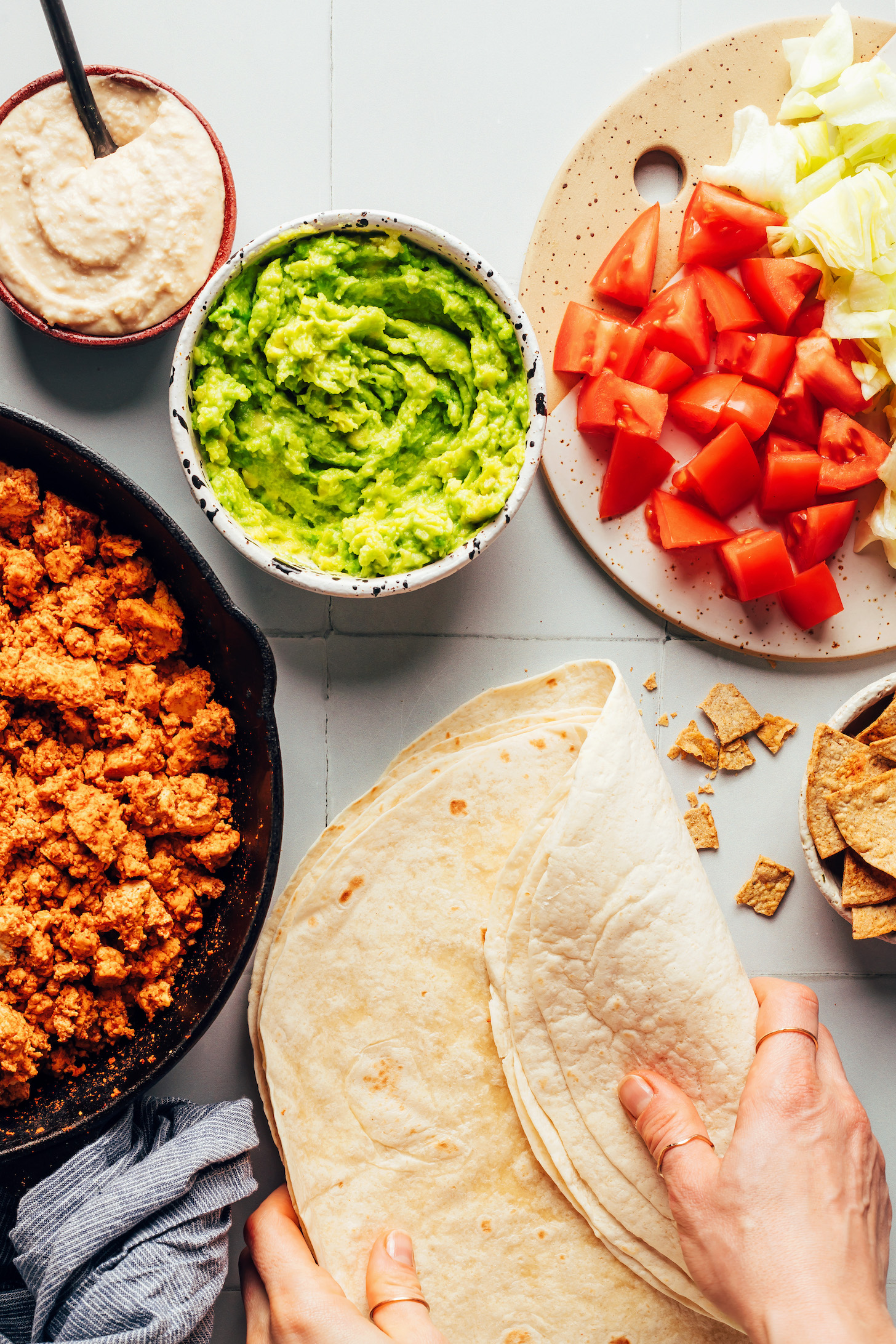 Tortillas, veggies, tofu taco meat, guacamole, and queso for making vegan crunchwrap burritos