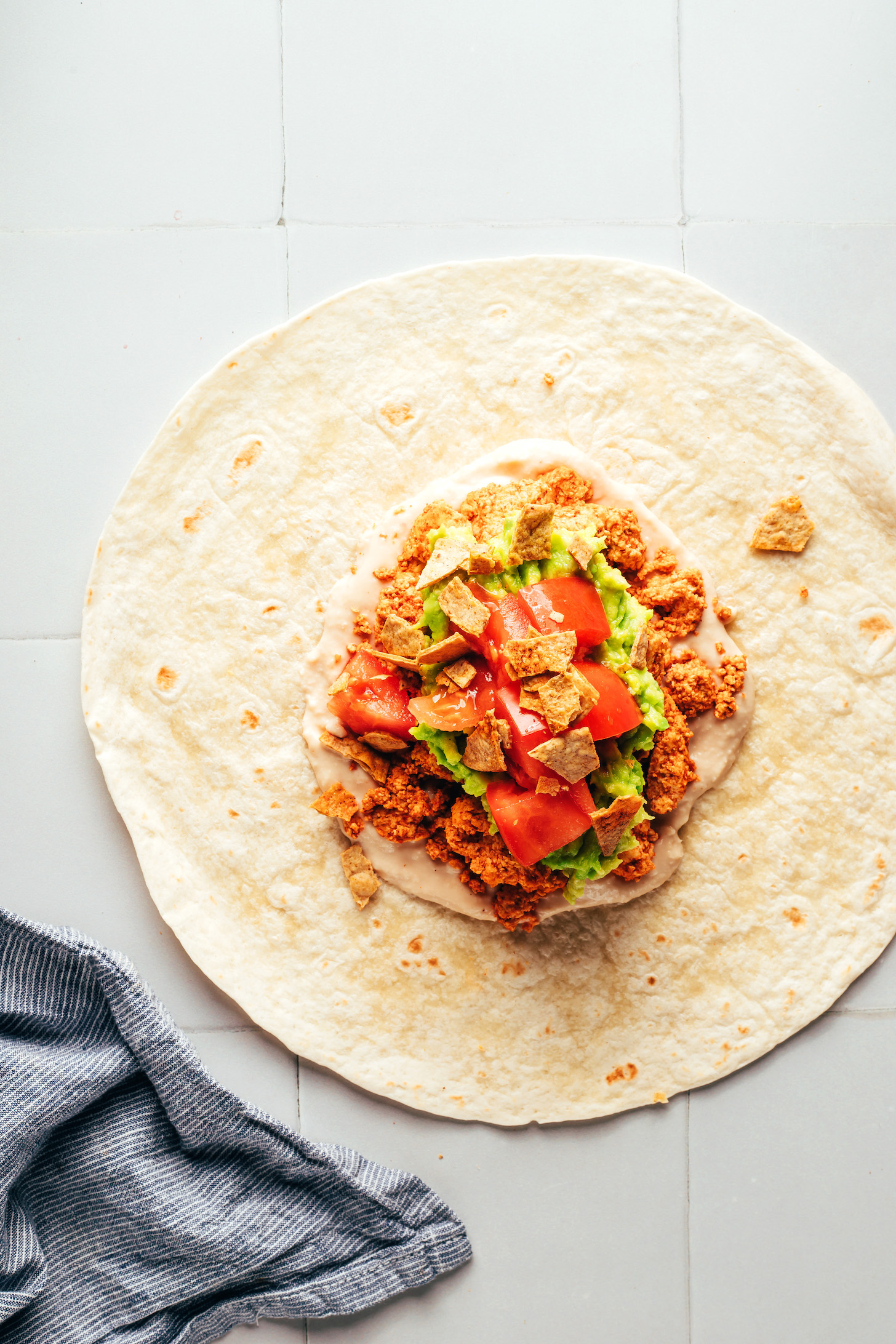 Flour tortilla layered with white bean queso, tofu taco meat, guacamole, tomatoes, and crushed tortilla chips