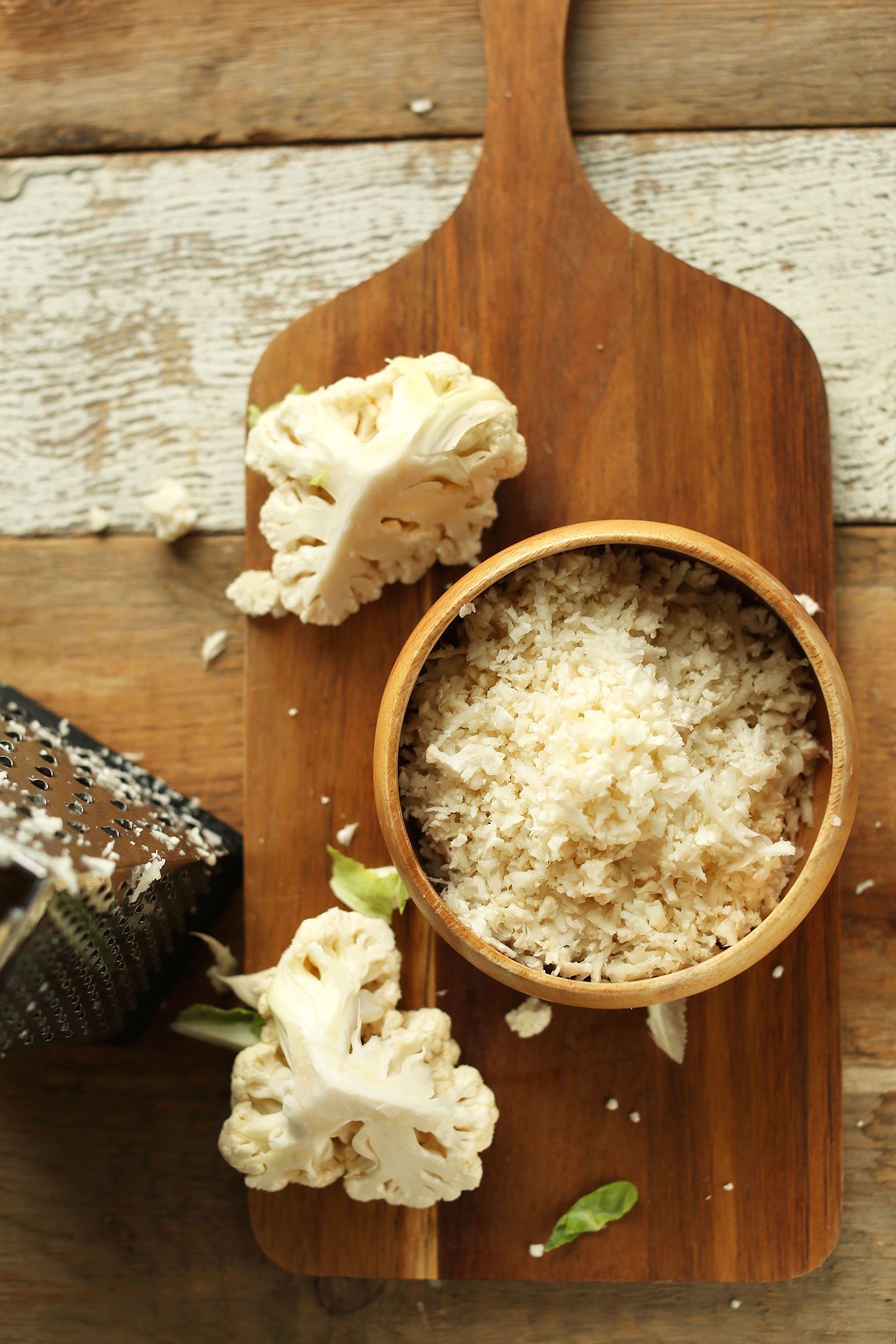 Bowl of cauliflower rice, a grater, and pieces of chopped cauliflower ready to be grated