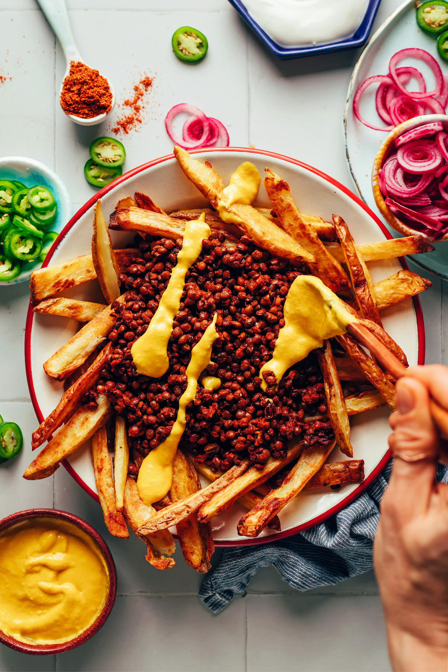 Drizzling vegan cheddar cheese over chili and fries