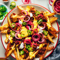 Bowl of vegan chili cheese fries topped with homemade vegan cheddar, jalapeño, and pickled onions