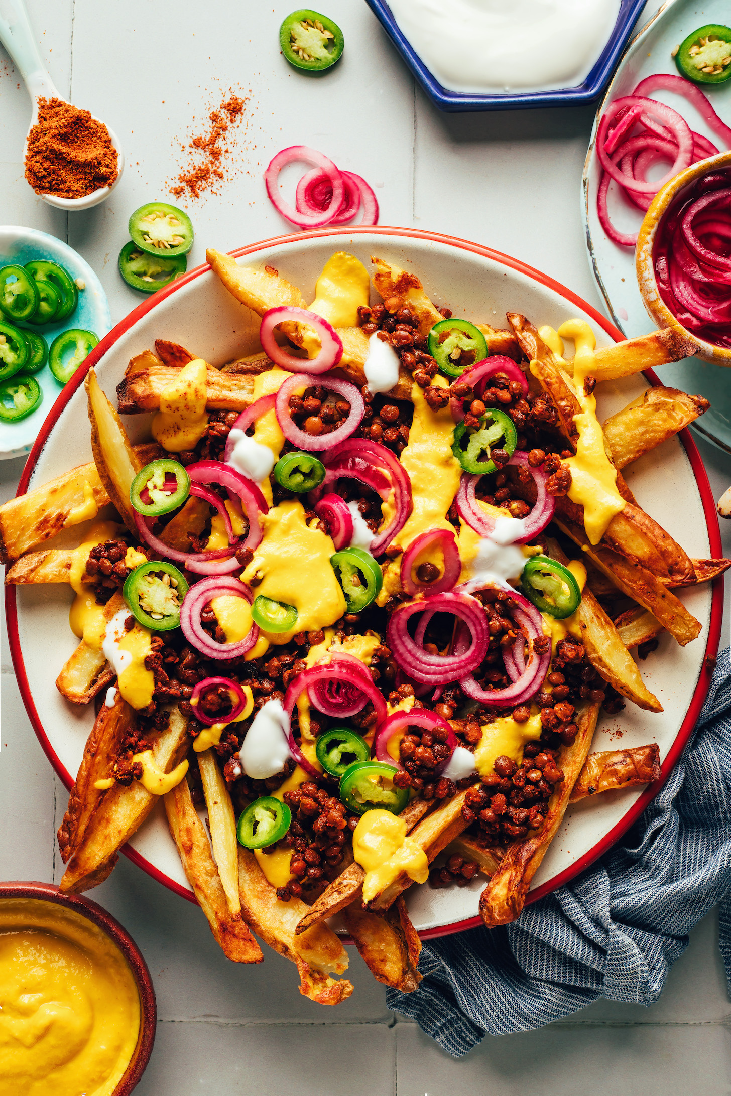 Large plate of vegan chili cheese fries topped with vegan cheddar cheese sauce, pickled red onions, vegan sour cream, and jalapeños