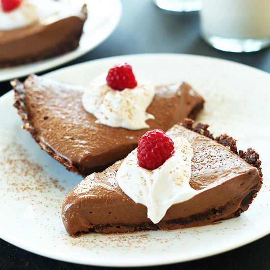 Plate with two slices of Vegan Chocolate Silk Pie topped with coconut whipped cream and raspberries