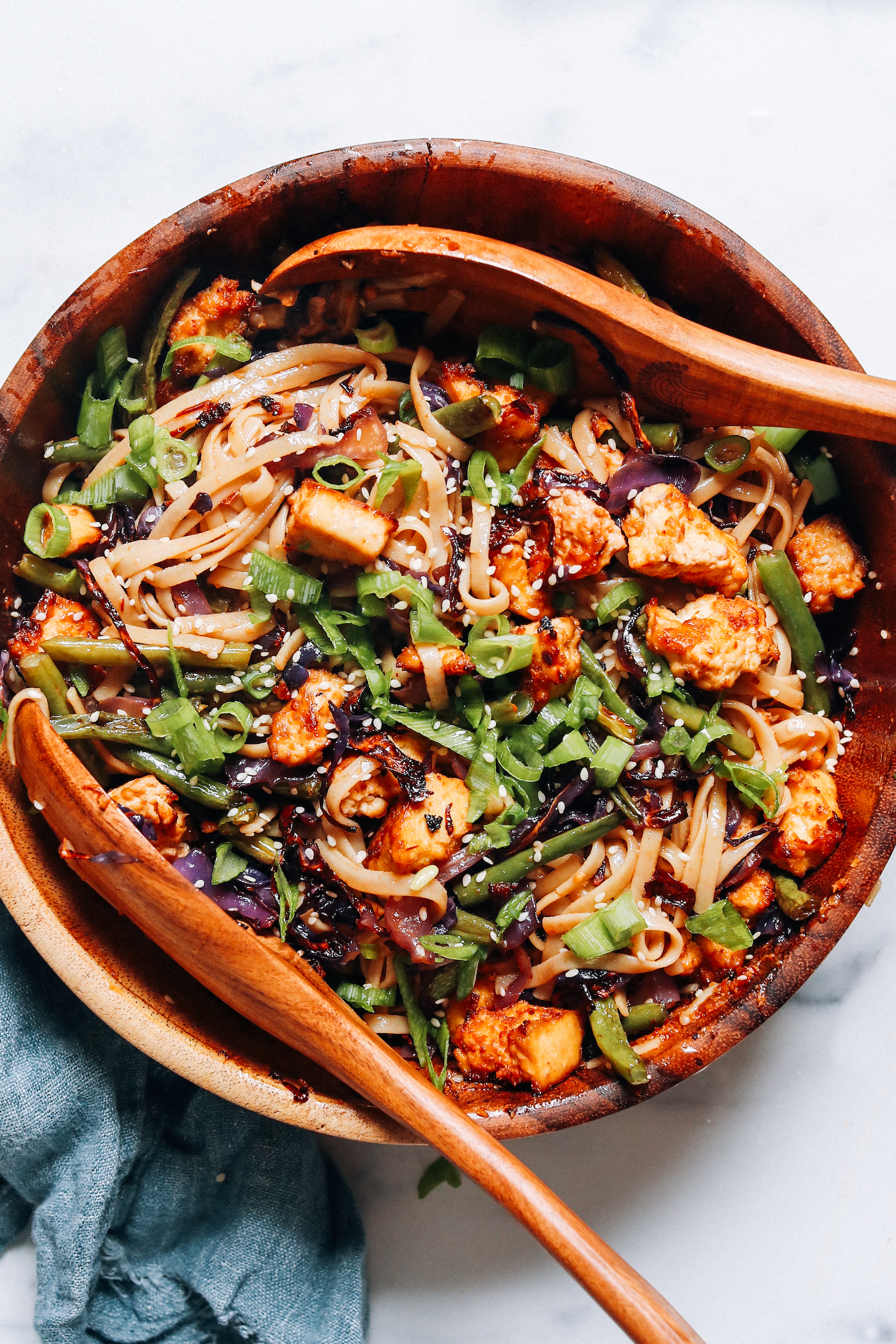 Wooden serving spoons in a bowl of sesame noodle tofu stir fry