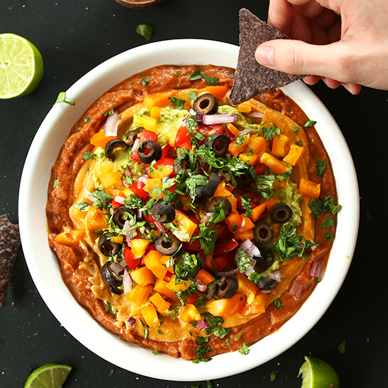 Blue corn tortilla chip ready to be dipped into a bowl of Vegan 7-Layer Mexican Dip