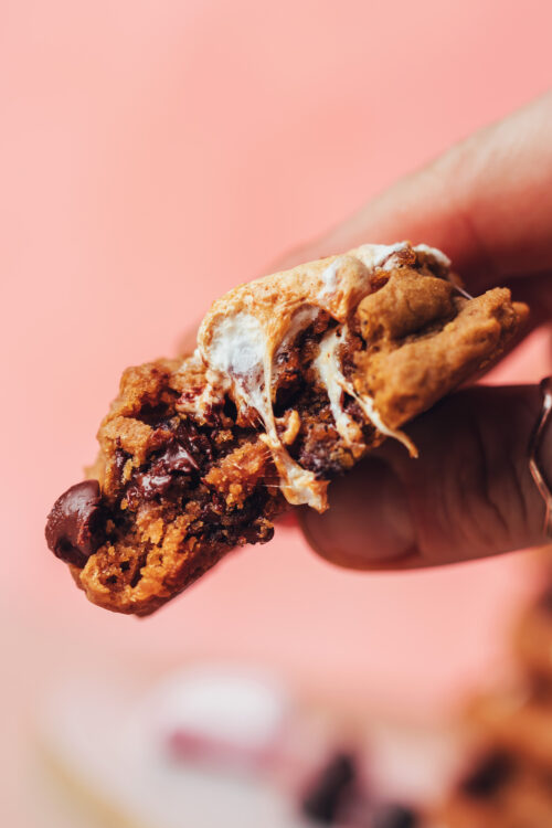 Holding a partially eaten s'mores cookies that shows the gooey marshmallows and melty chocolate