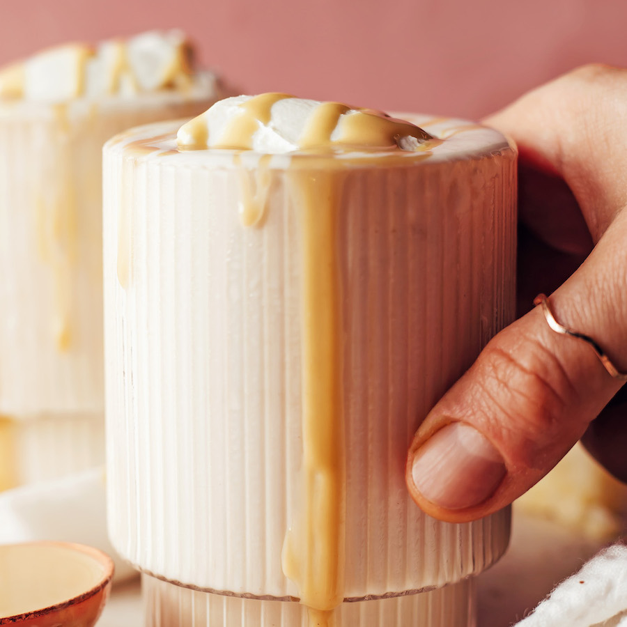 Hand holding the side of a glass filled with our vanilla tahini shake recipe